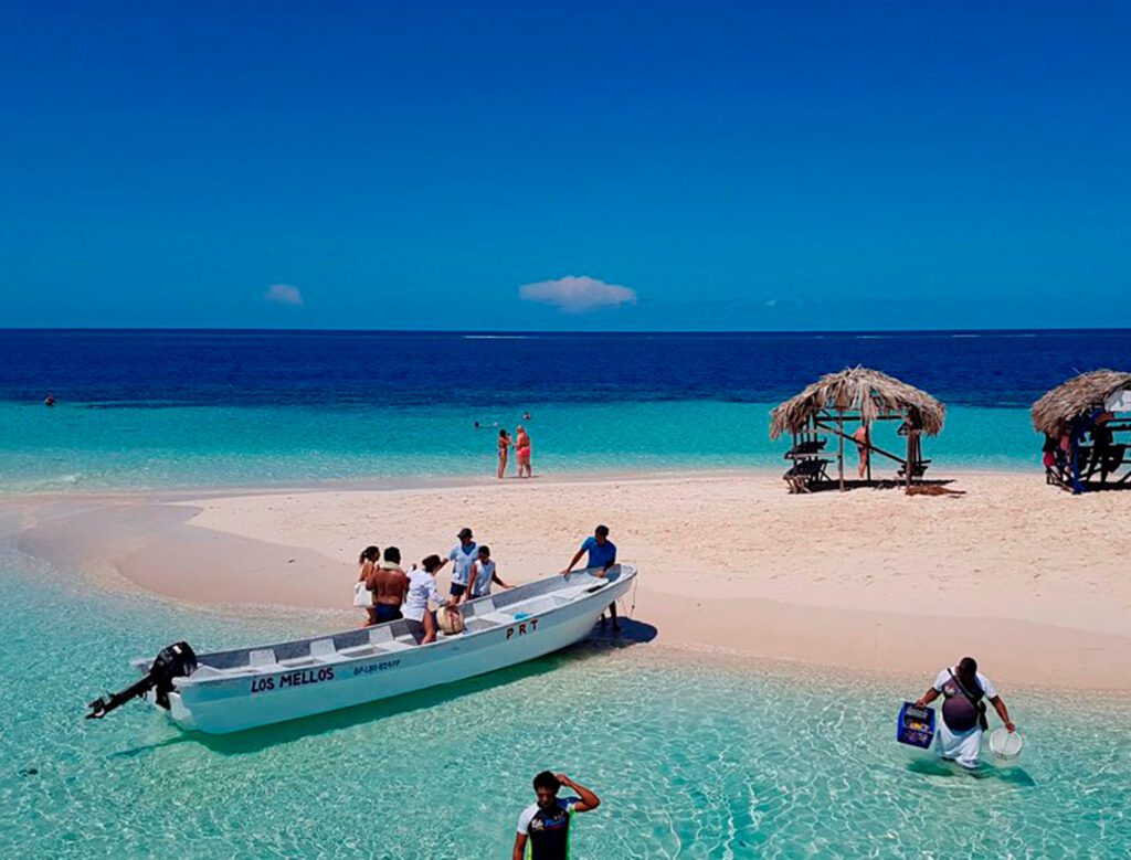 Turistas llegando en lancha a Cayo Arena, mostrando las casetas de paja típicas en la arena.