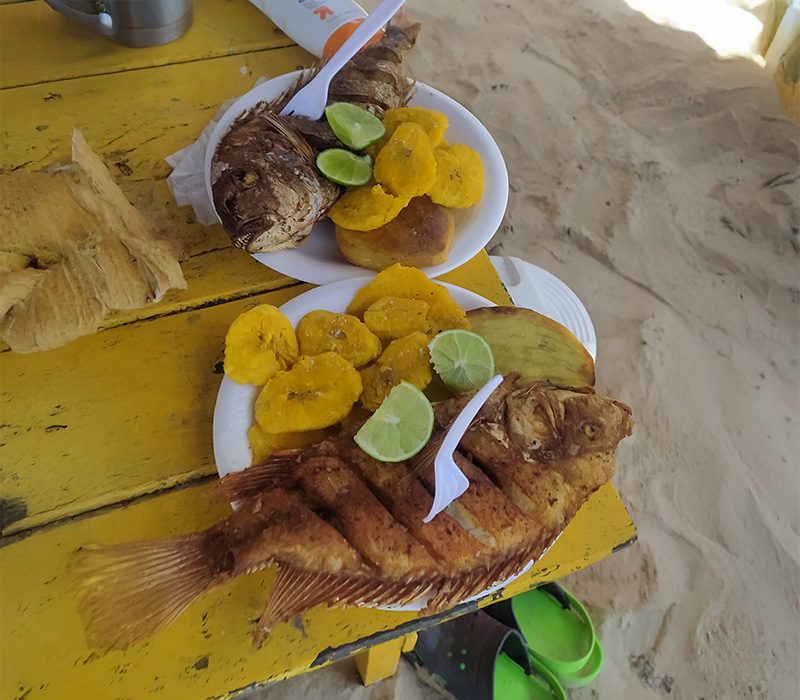 Servicio de pescado frito típico de Boca Chica con tostones, yaniqueque y limón servido en mesa de playa.