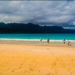 Vista panorámica de Playa Rincón en Samaná con turistas disfrutando de sus aguas turquesas y tranquilas. Al fondo se ven las montañas de la península.