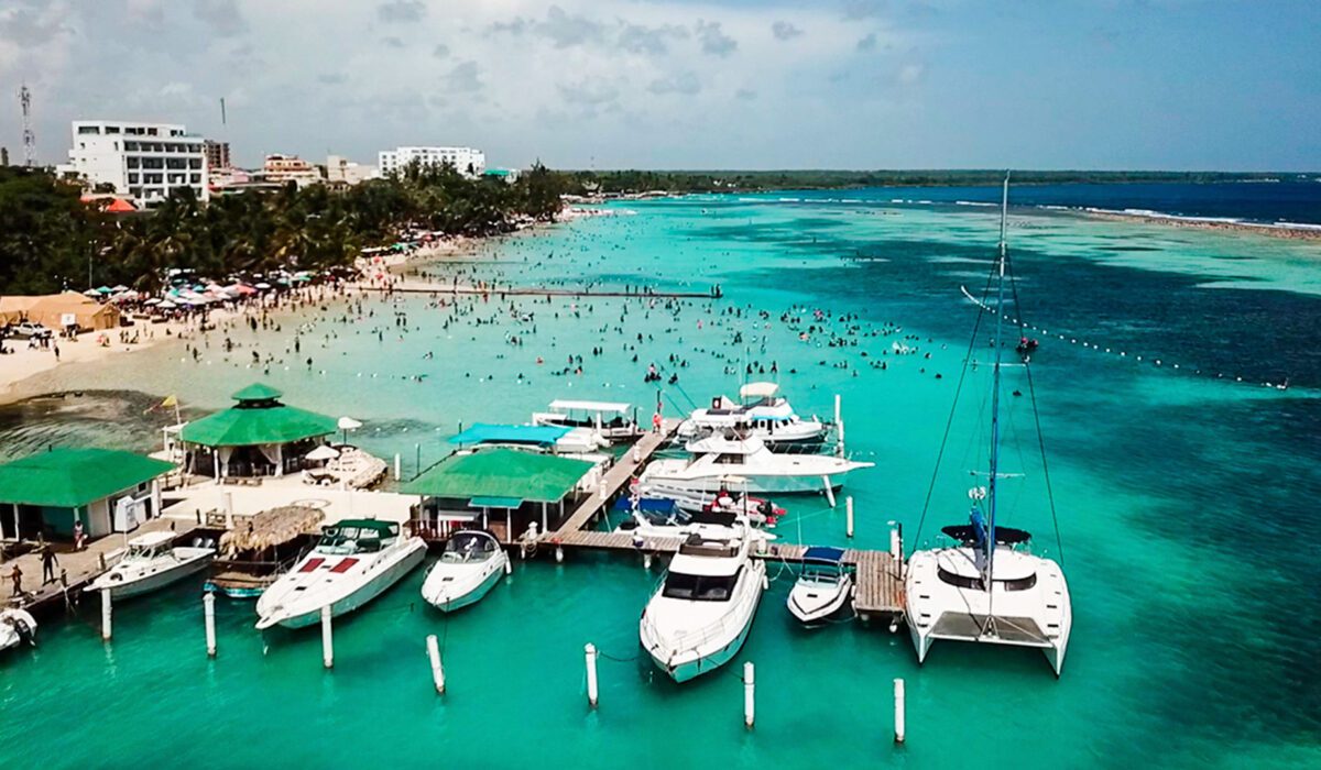 Vista aérea de Playa Boca Chica mostrando sus aguas turquesas poco profundas, llena de bañistas y yates en la marina.