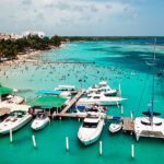 Vista aérea de Playa Boca Chica mostrando sus aguas turquesas poco profundas, llena de bañistas y yates en la marina.
